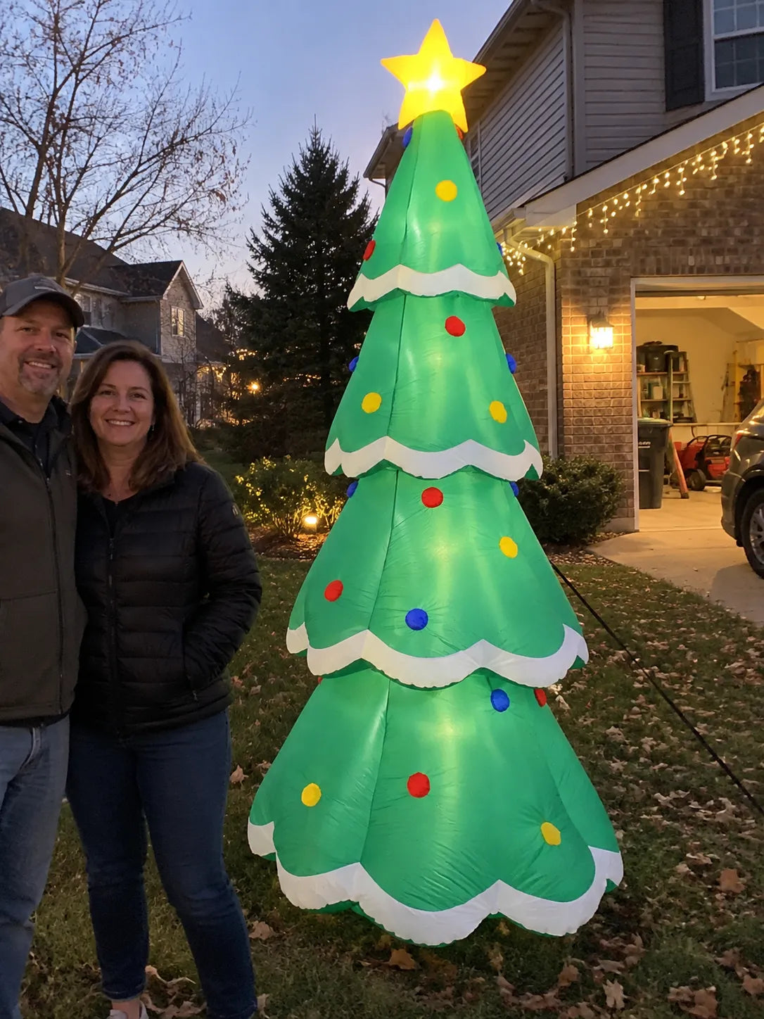 Couple beside an illuminated inflatable tree in their yard