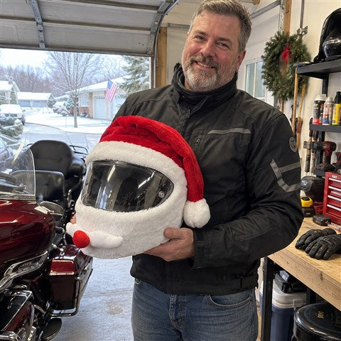 Rider holding a Santa-style covered helmet in a home garage