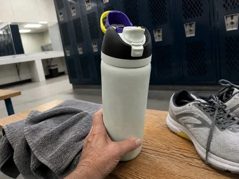 Pale glow-in-the-dark bottle on a gym bench beside a towel and shoes