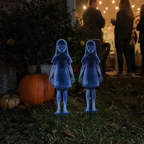 Two ghost-girl stakes near pumpkins during a backyard Halloween gathering