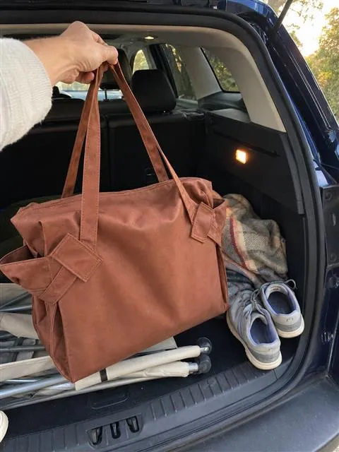 Brown tote being lifted from an SUV trunk
