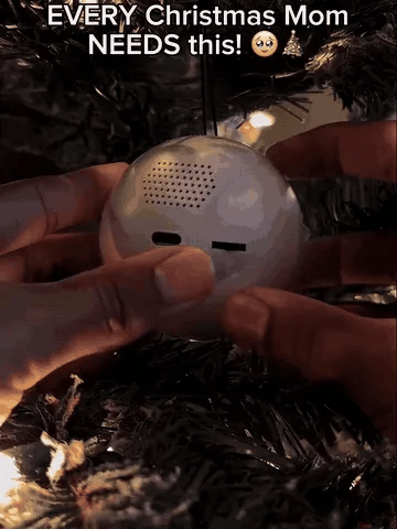 A hand turning on and hanging the MemoryGlow video keepsake orb on a Christmas tree