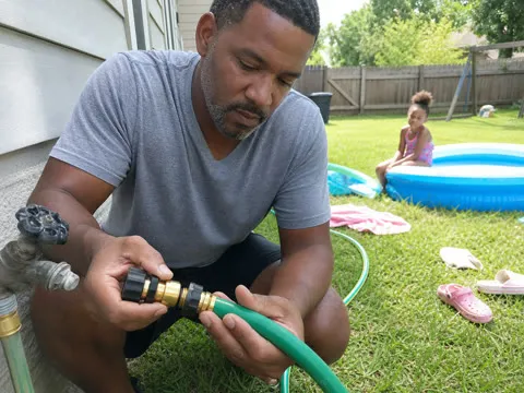 Father connecting a hose near a backyard pool