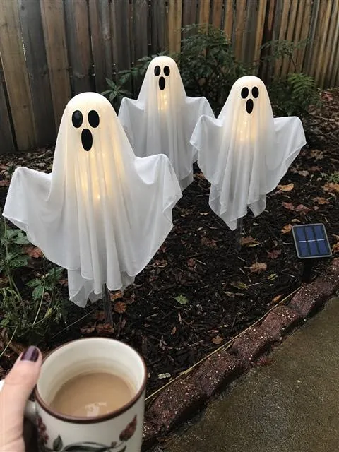 Three solar ghost lights standing in a damp backyard garden after light rain