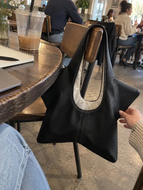 Black star-shaped tote hanging from a cafe chair beside a notebook and iced coffee