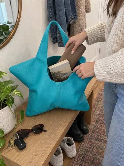 Turquoise star-shaped tote being packed with a wallet and paperback on an entryway bench