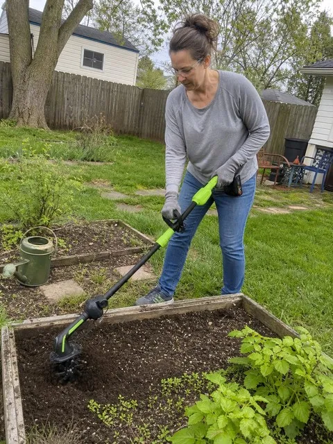 Gardener using the cordless tiller in a raised bed