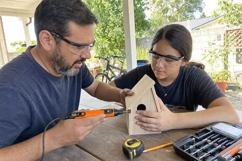 Family birdhouse sanding project on a home patio