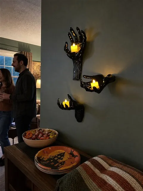 Three glowing black hand candle holders beside a Halloween snack table