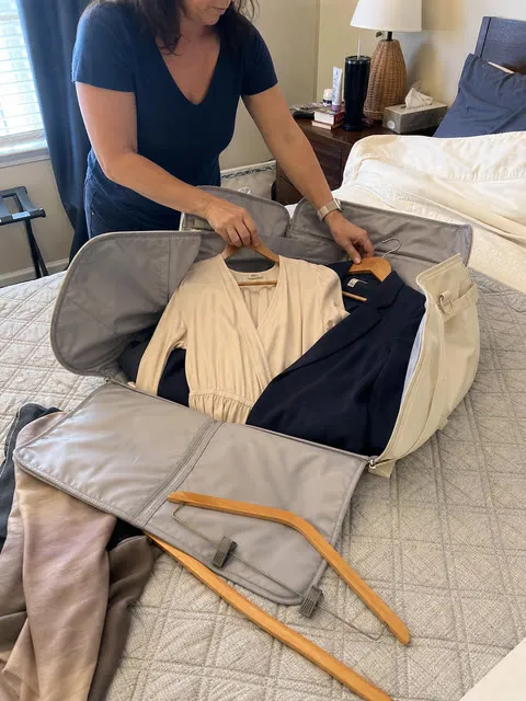 Traveler arranging a dress and blazer in the open garment bag