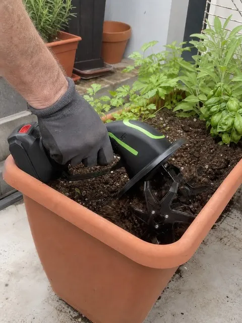 Handheld cordless tiller working inside a patio planter