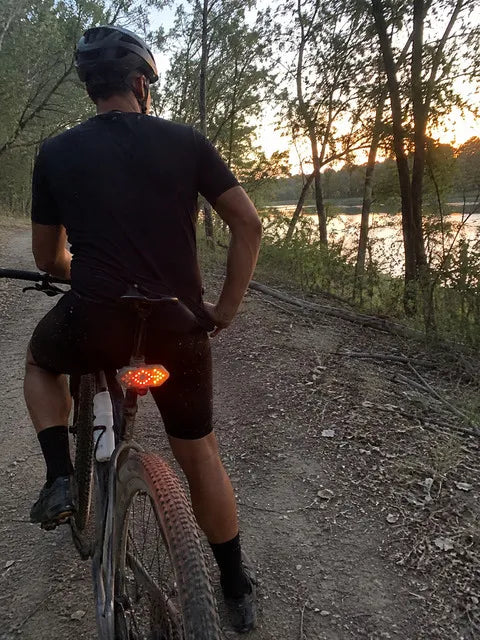 Cyclist using a bright rear directional light on a sunset trail ride