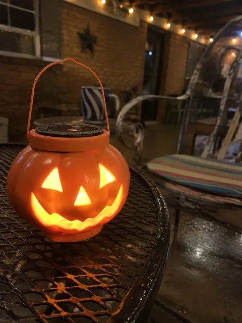 Glowing pumpkin solar lantern on a covered patio table after rain