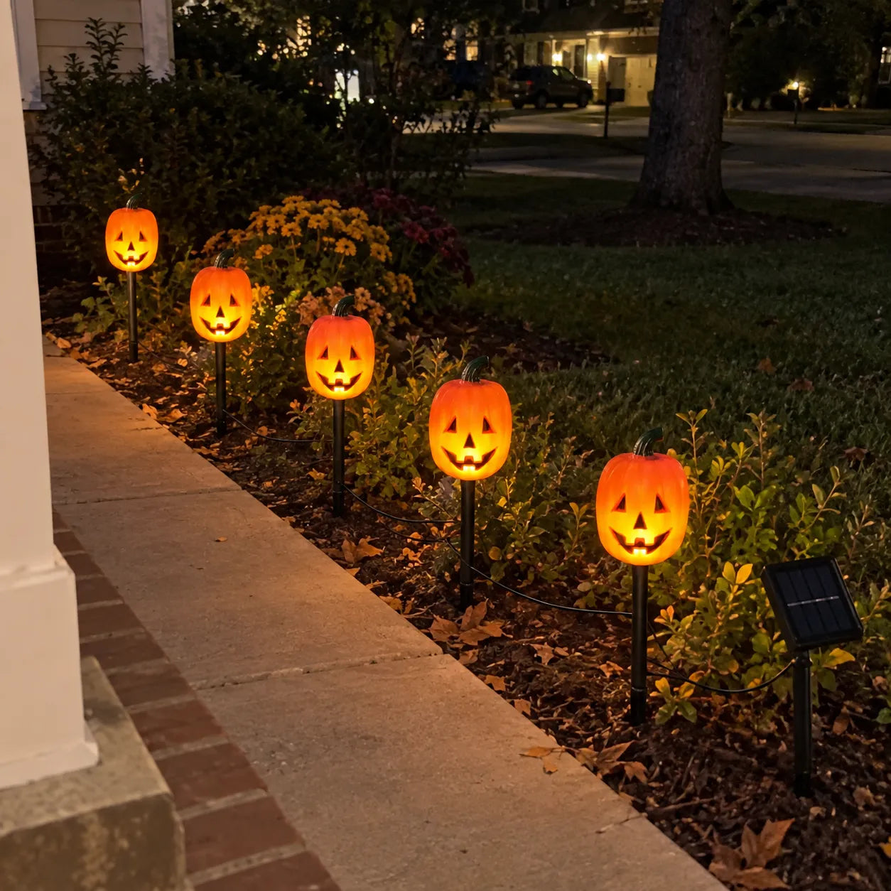 Five glowing pumpkin lights beside a front walkway at night