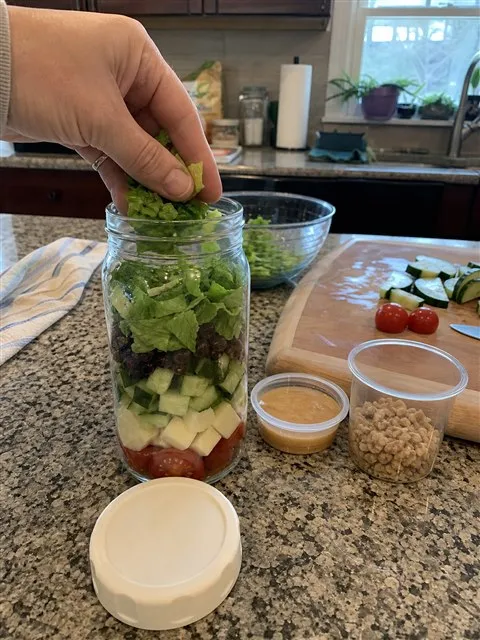 Layered salad jar being packed on a home kitchen counter