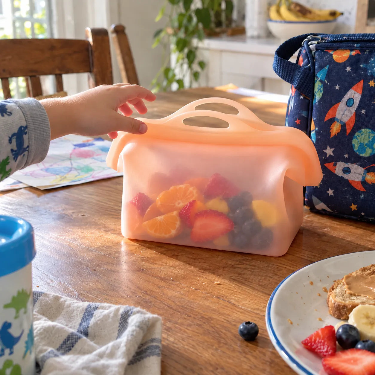 Child reaching for fruit stored in the silicone bag beside a lunch tote