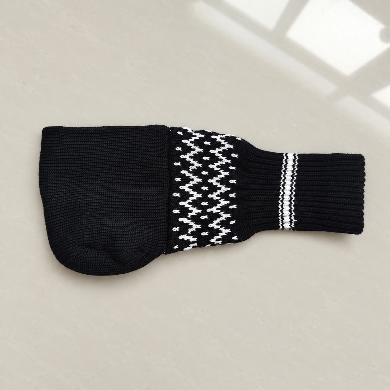 Black knitted beer mitten laid flat to show the connected sleeve and cuff
