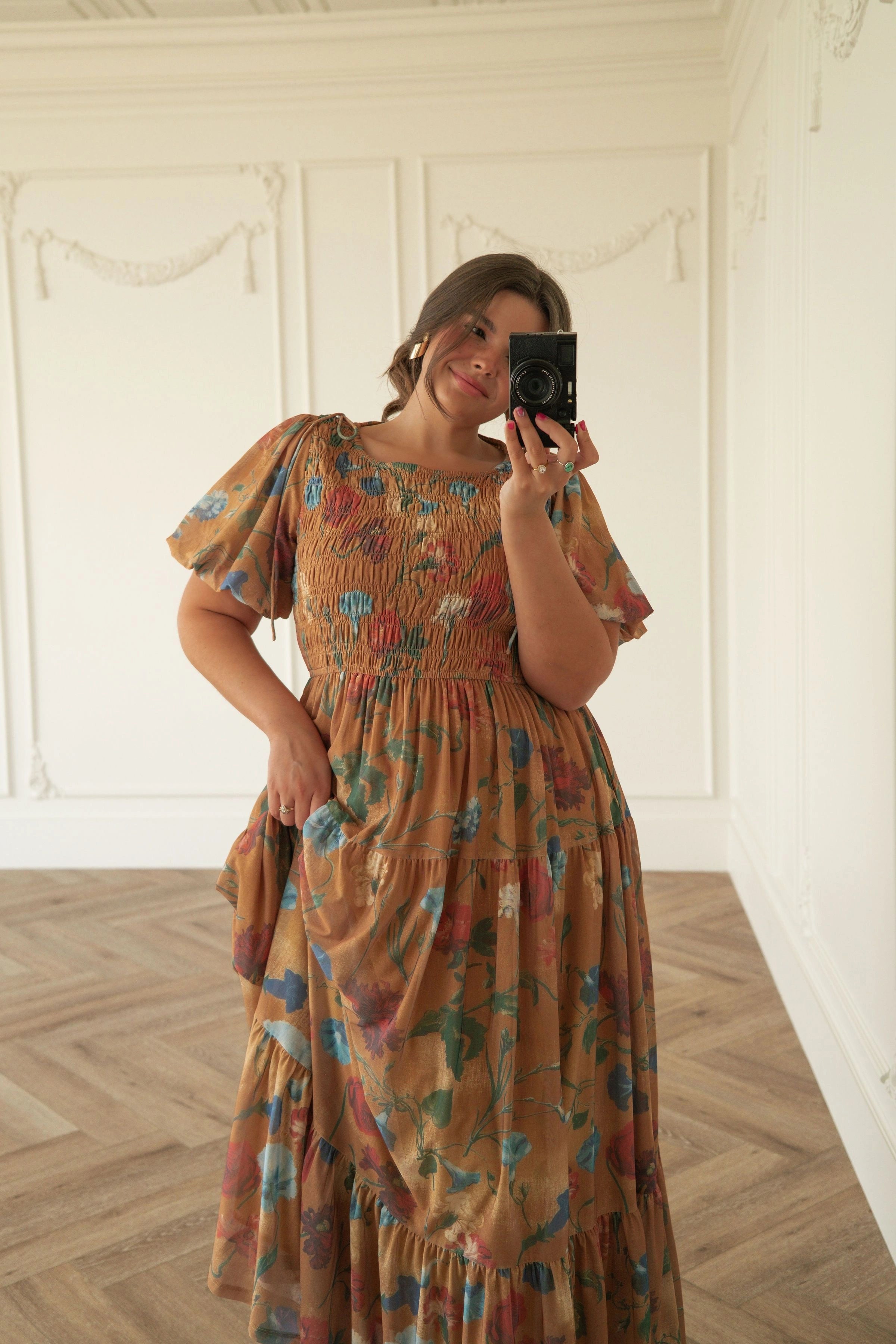 The image shows a woman taking a selfie in front of a mirror, wearing a beautiful dress from the 2015 Spring/Summer collection. She is standing on the floor, holding a camera in her hands, with a