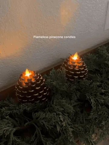 Two flameless pinecone candle lights switched on and glowing in seasonal greenery