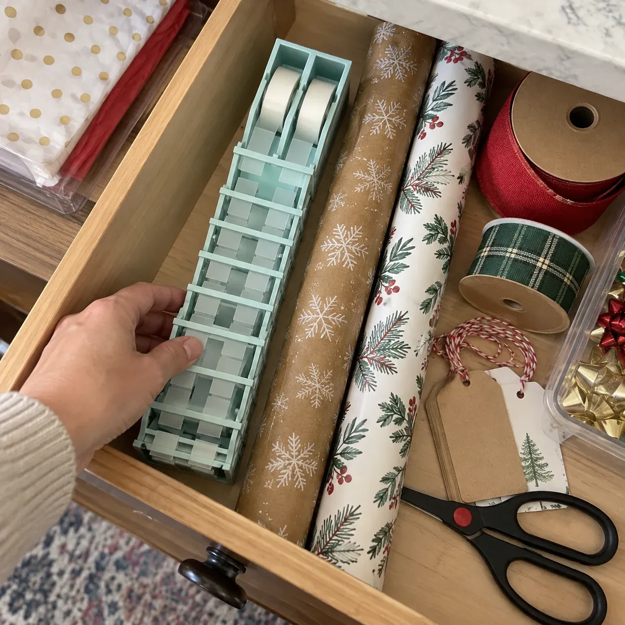 Retracted tape prep station stored in a drawer beside wrapping paper, ribbon, tags, and scissors