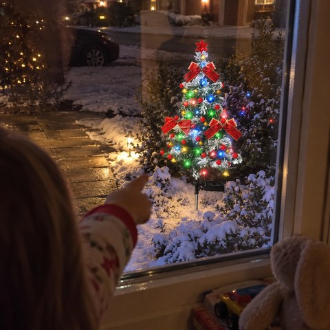 Barn ser gennem et vindue på et lysende juletræ på spyd