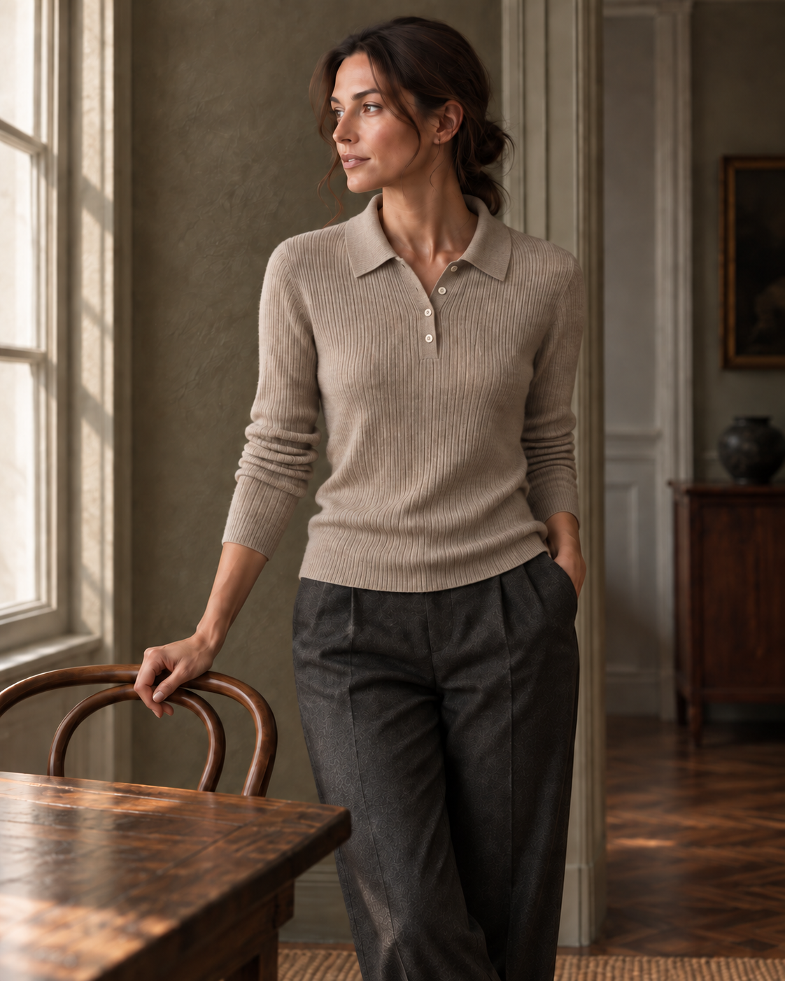 The oatmeal Ribbed Polo styled with charcoal trousers beside a window. Editorial styling view.