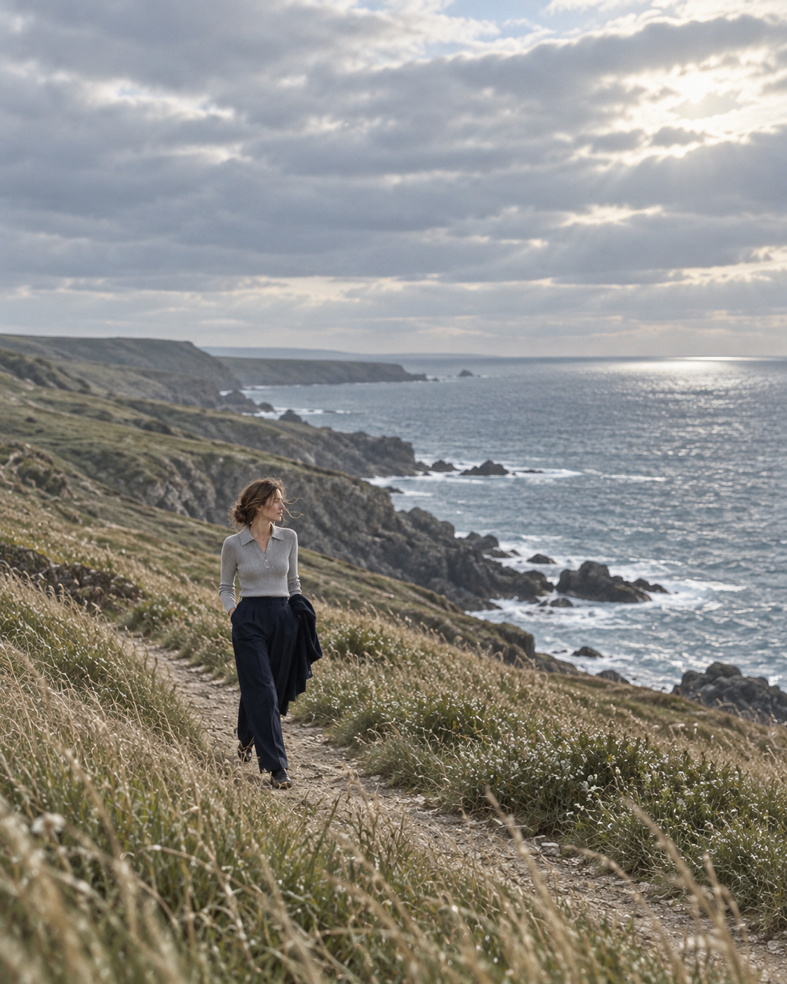 A distant figure walks above a rocky coast.
