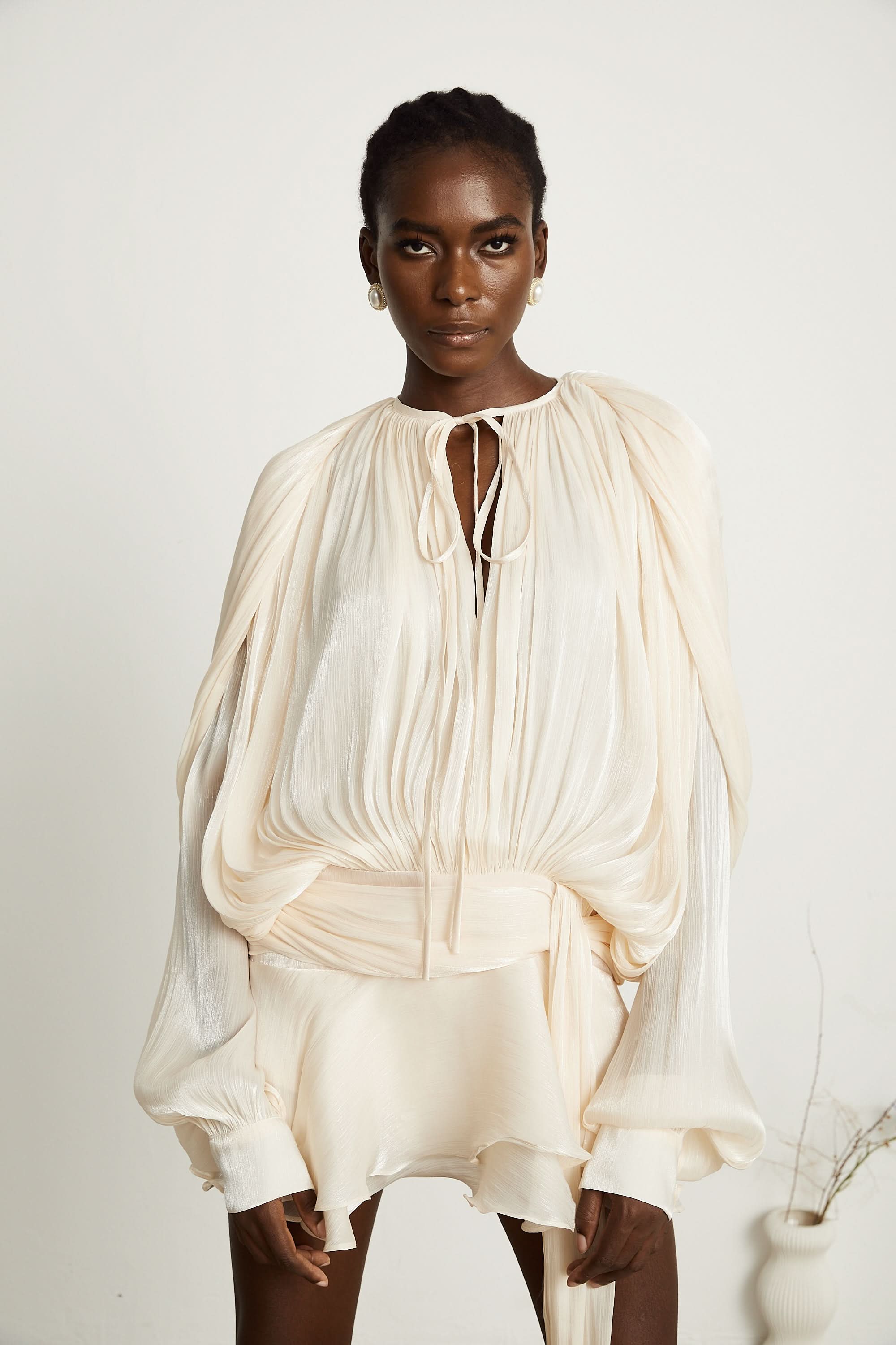 Cream pleated mini dress with tie-neck closure and voluminous sleeves