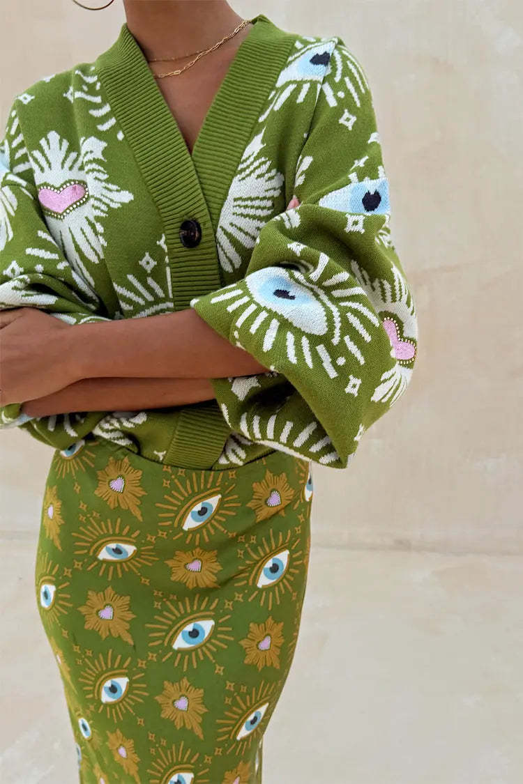 Close-up of green knit cardigan showing white eyelash pattern with blue eye and pink heart embroidery