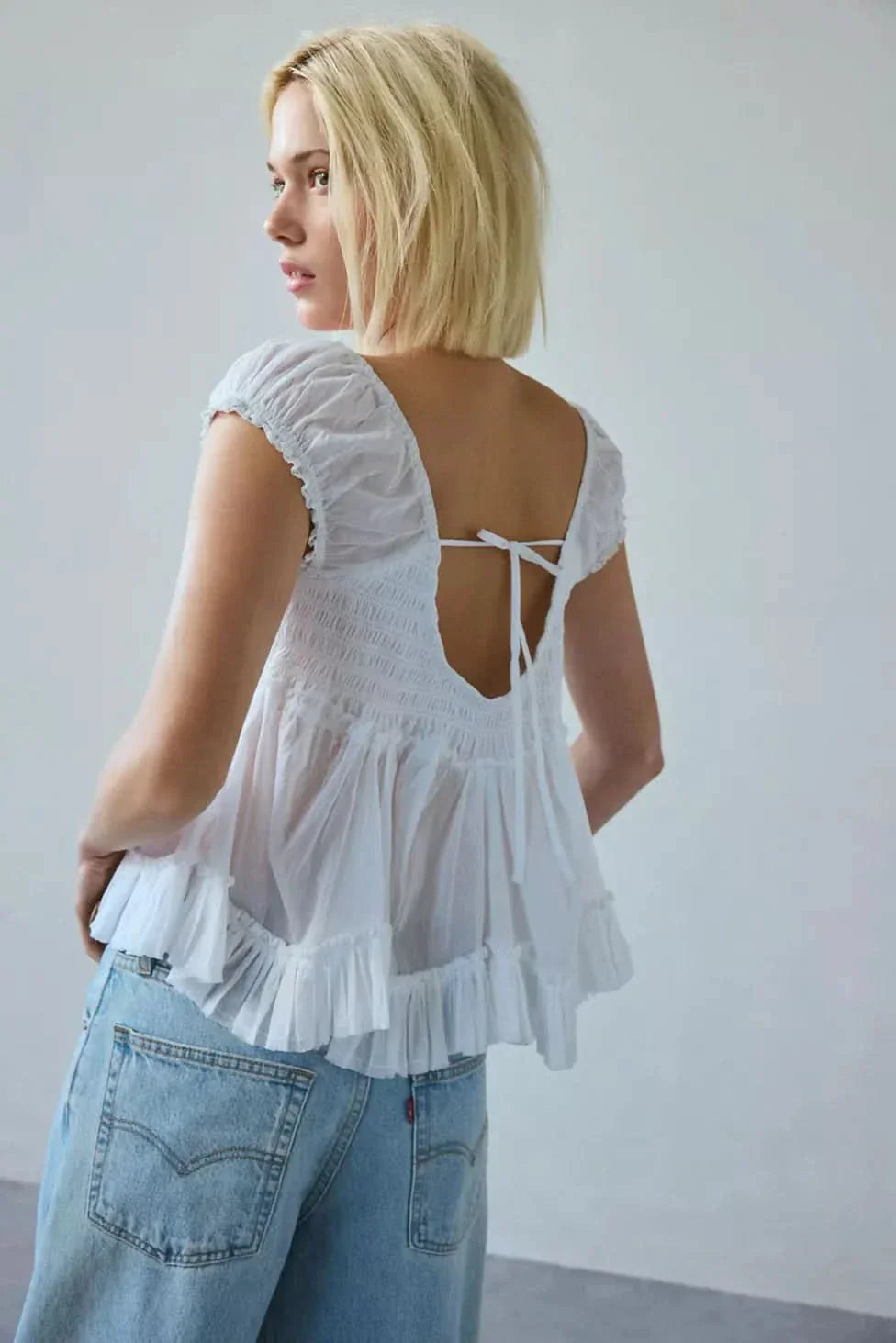 Tie-back detail on white lace top showing smocked bodice and open back design