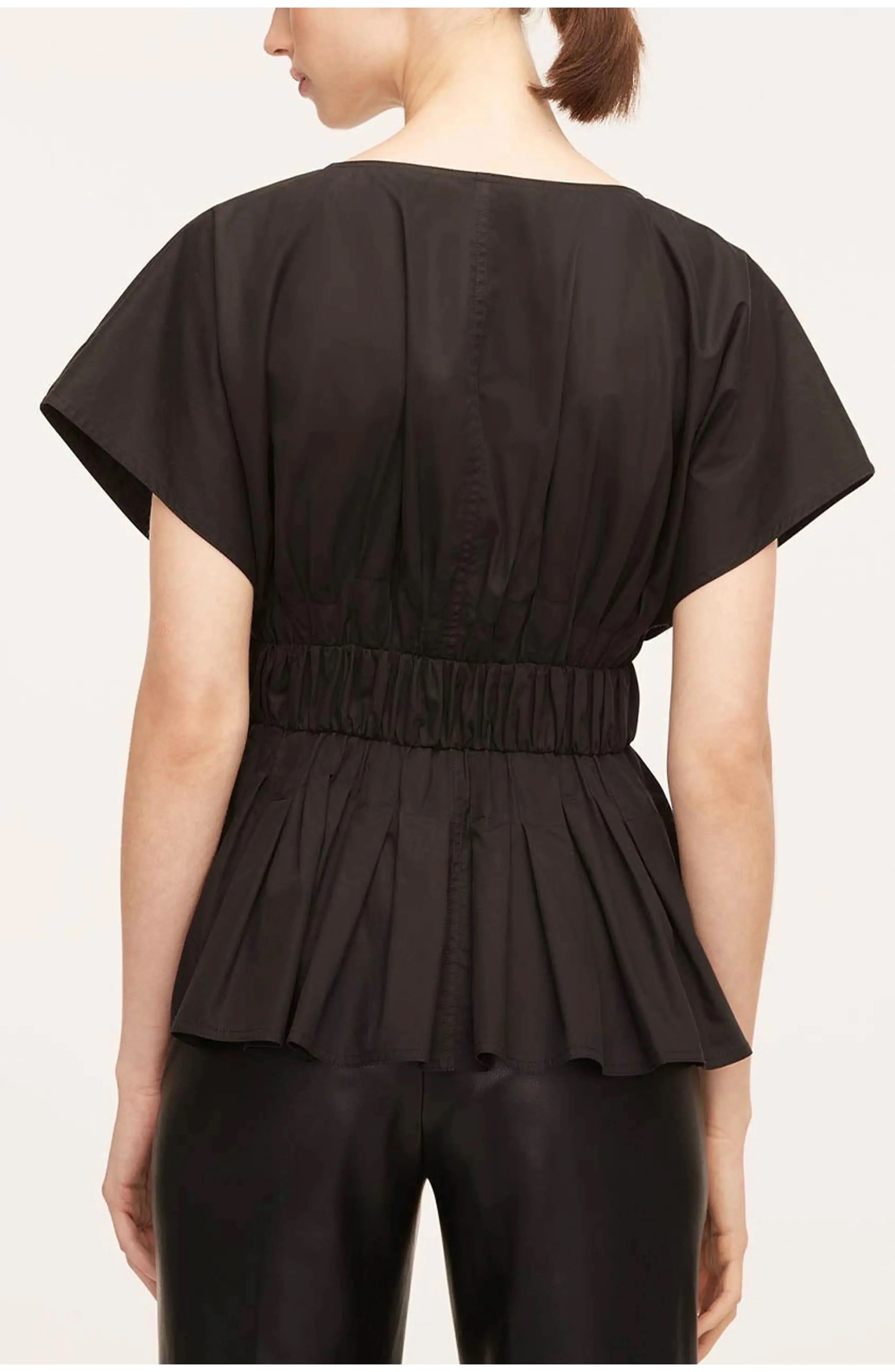 Back view of black pleated peplum blouse with tailored seaming and peplum flare