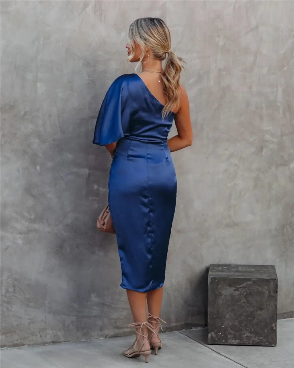Front view of navy blue draped midi dress with dramatic one-shoulder cape and side slit detail