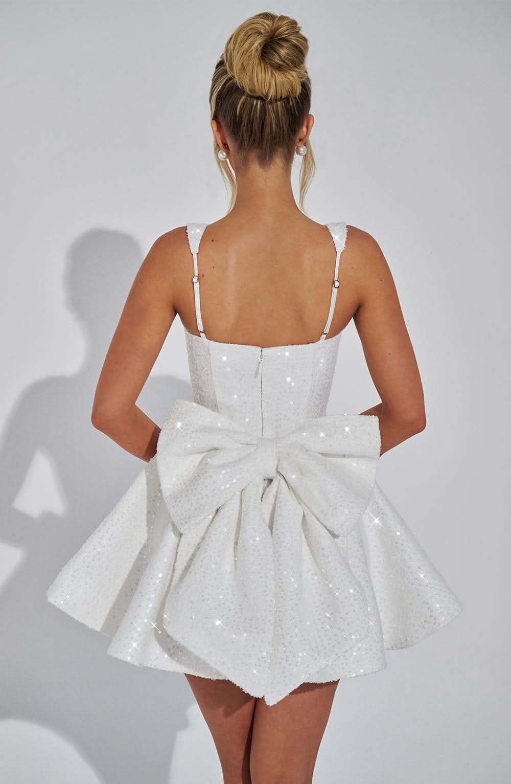 Back view of white sequin dress with zip closure and bow detail