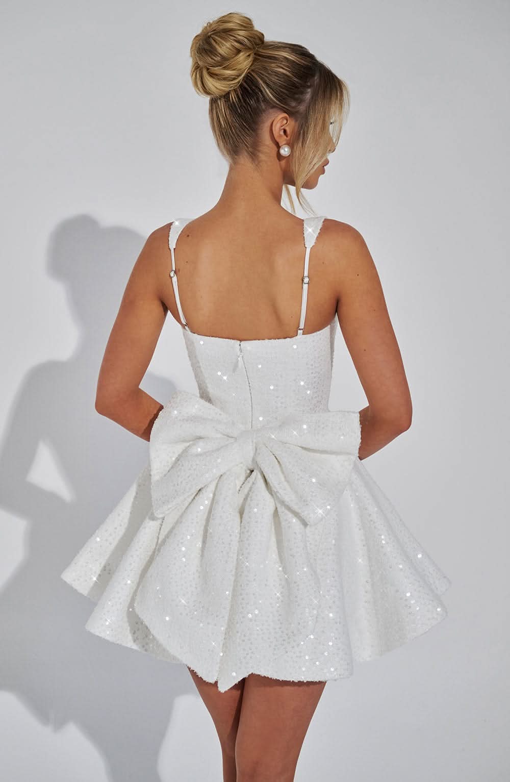 Side back view of white sequin mini dress with structured bow