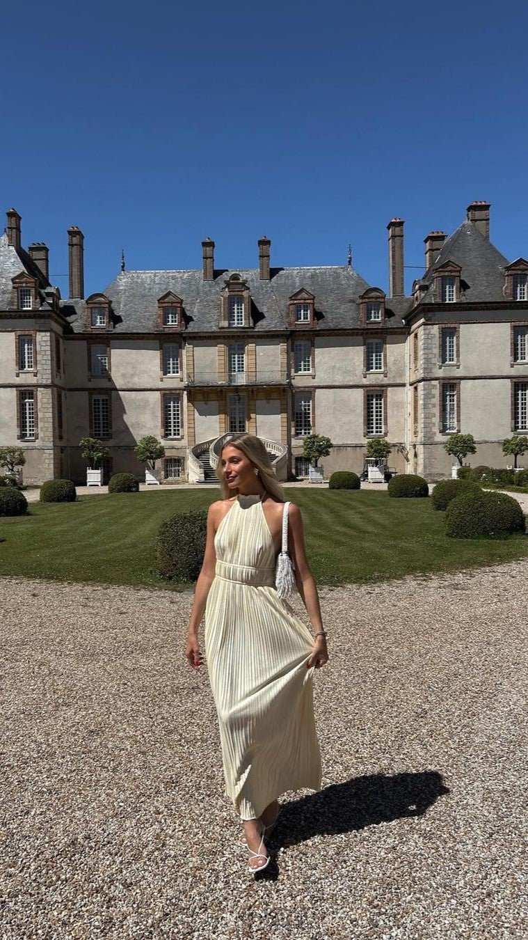 Cream pleated maxi dress worn outdoors in front of stone chateau