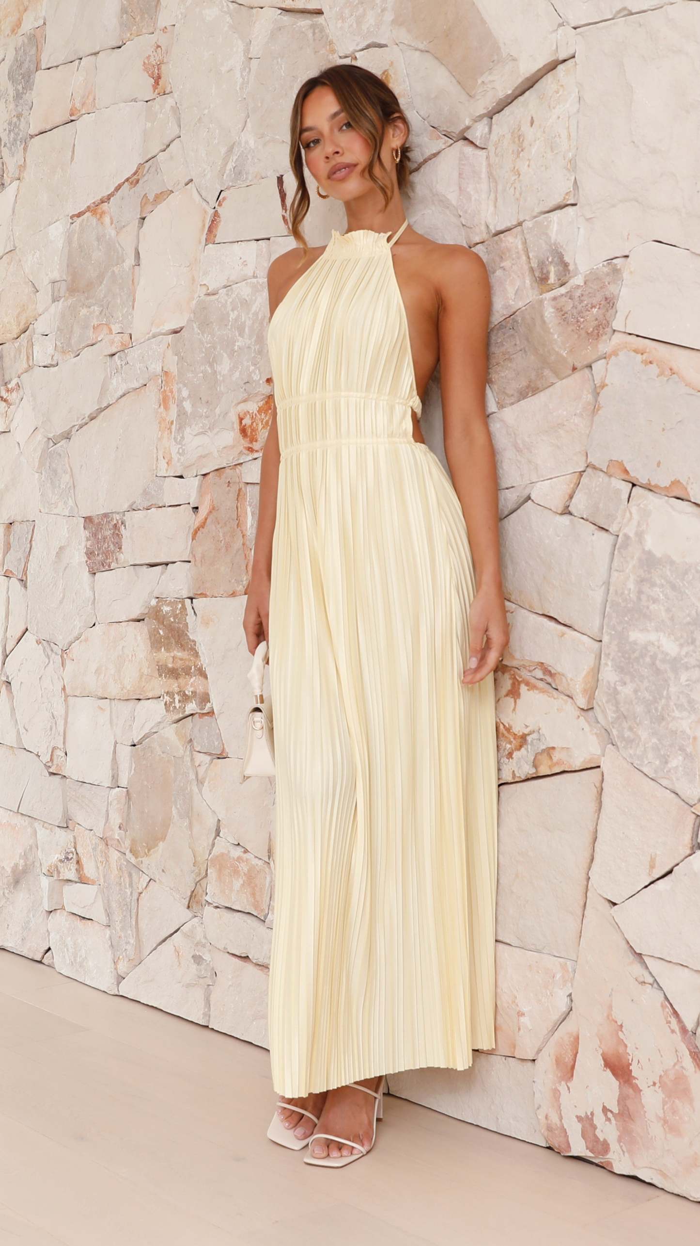 Cream pleated halter maxi dress with cinched waist worn with white sandals