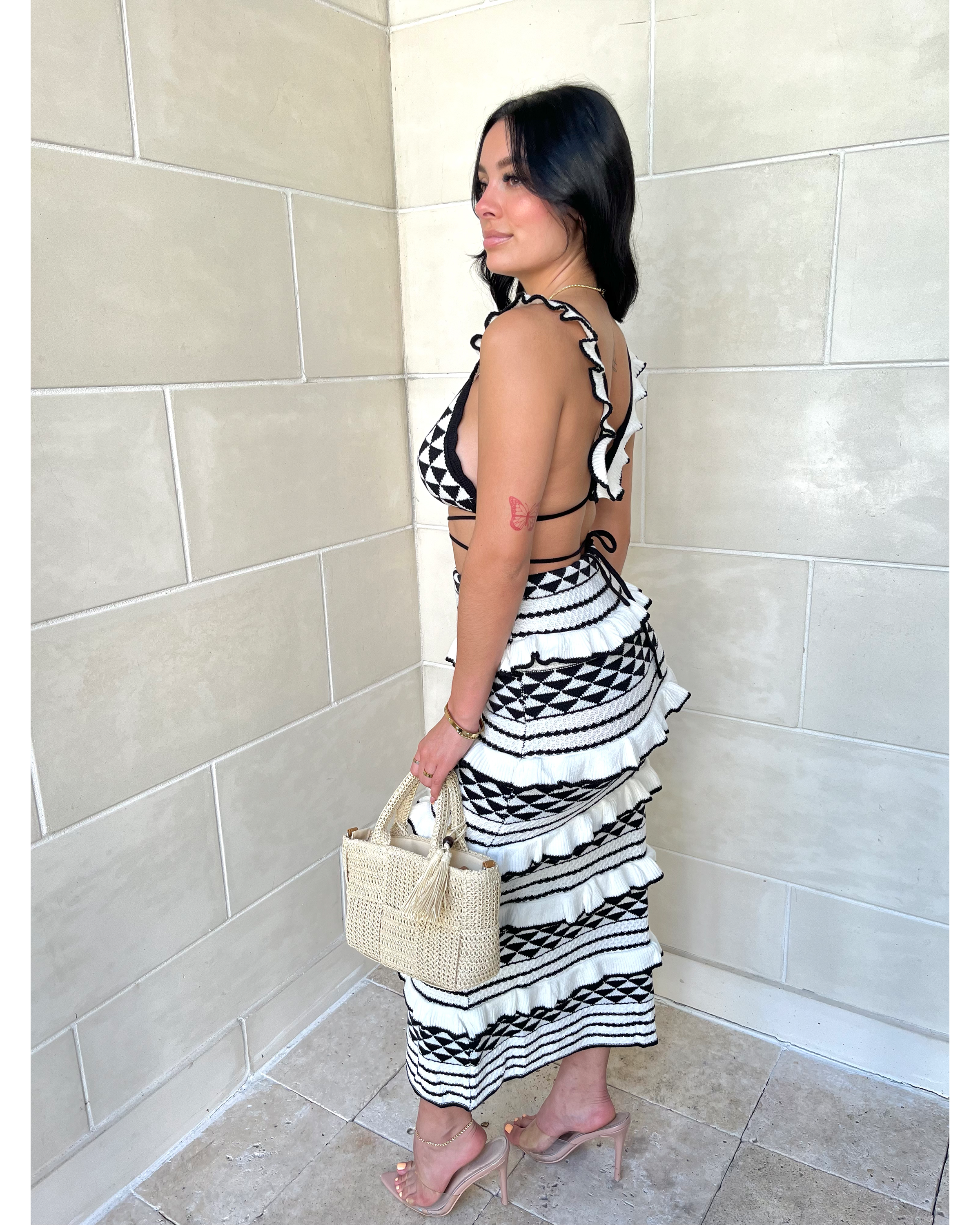 Side profile of geometric knit set showing cross-back crop top and tiered midi skirt detail