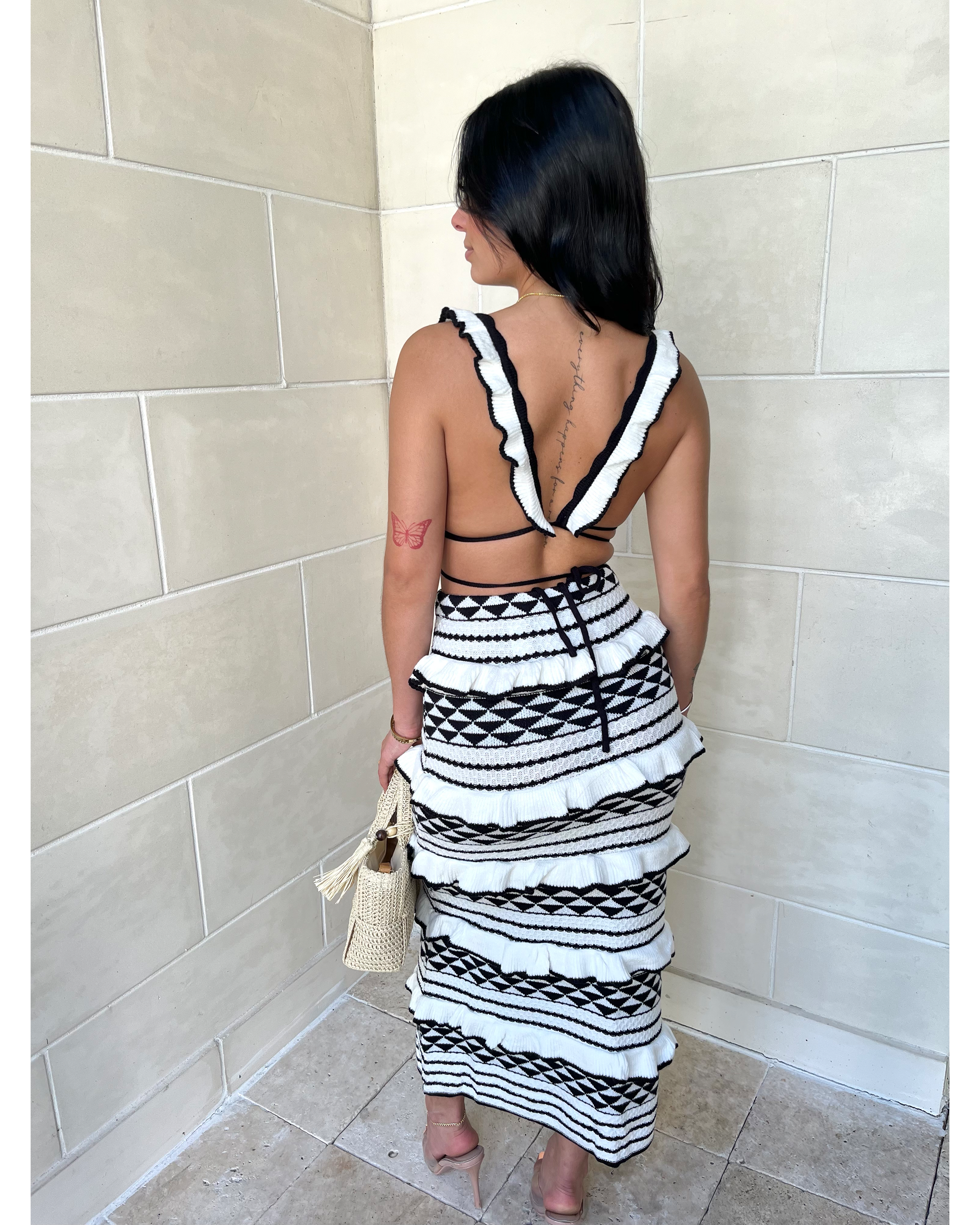 Back view of geometric knit crop top with white trim straps and patterned midi skirt