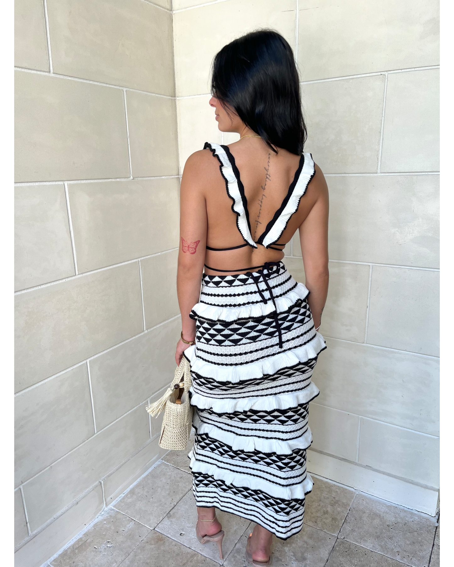 Back view of geometric knit crop top with white trim straps and patterned midi skirt