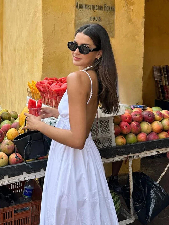 White maxi vacation dress with deep V-neck and backless silhouette, side profile view