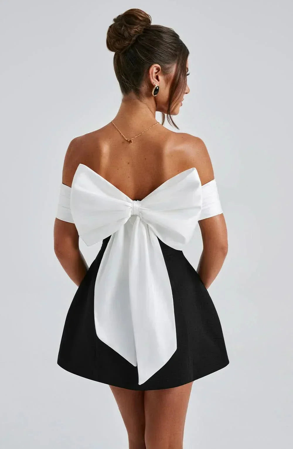 Back view of black mini dress with large white bow detail and off-shoulder sleeves