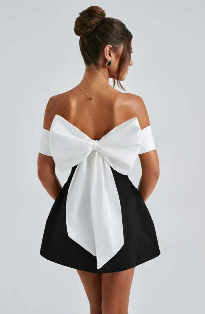 Back view of black mini dress with large white bow detail and off-shoulder sleeves