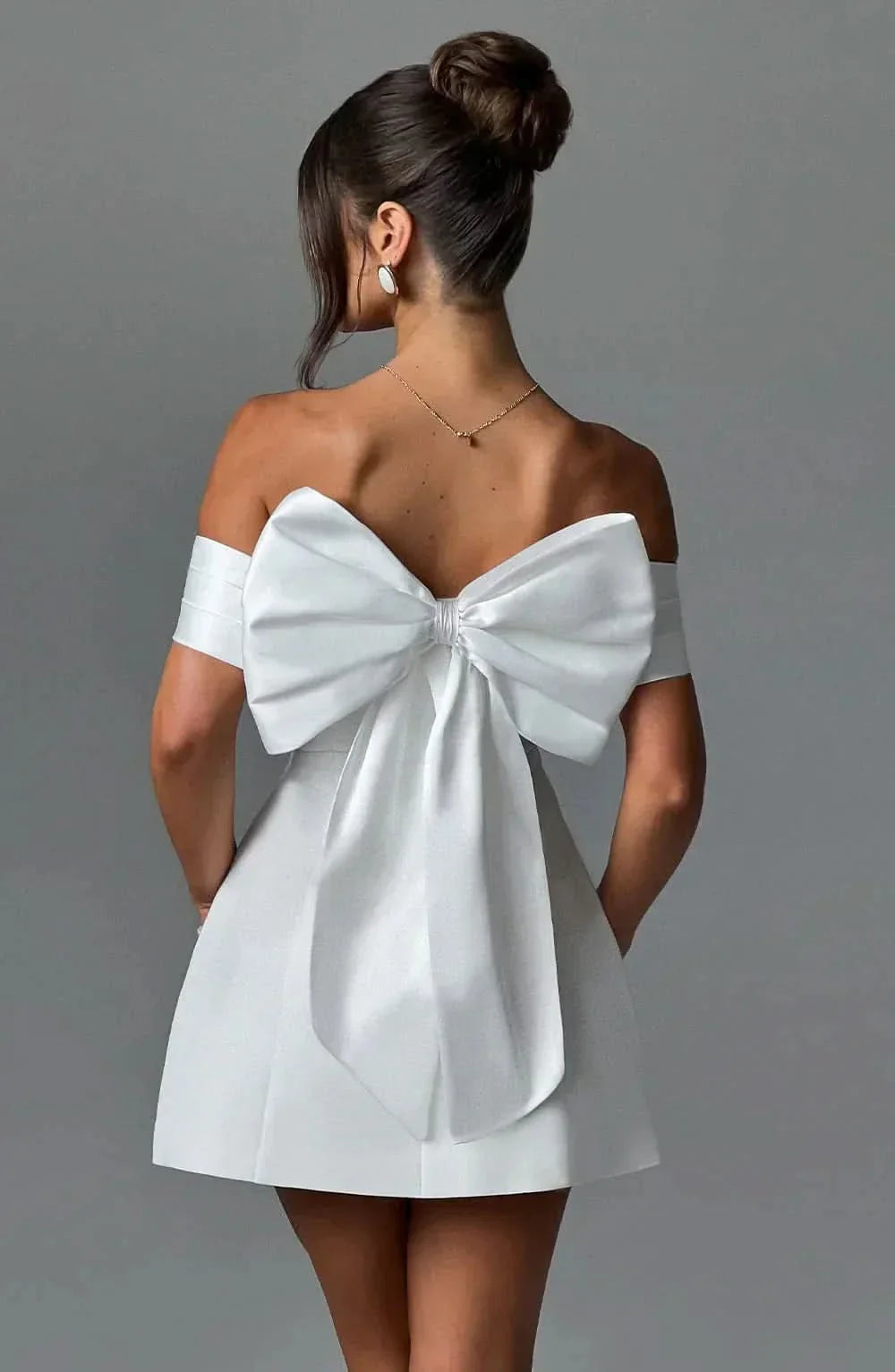 Back view of white mini dress with large bow detail and draped off-shoulder design