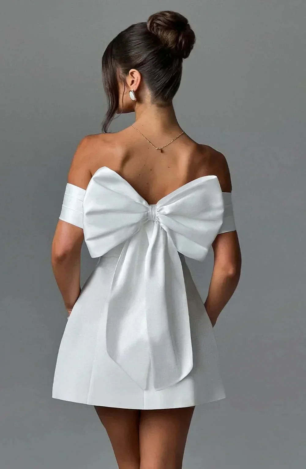 Back view of white mini dress with large bow detail and draped off-shoulder design
