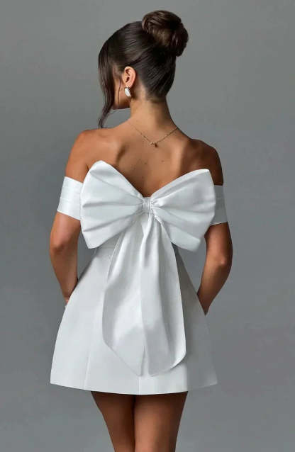 Back view of white mini dress with large bow detail and draped off-shoulder design