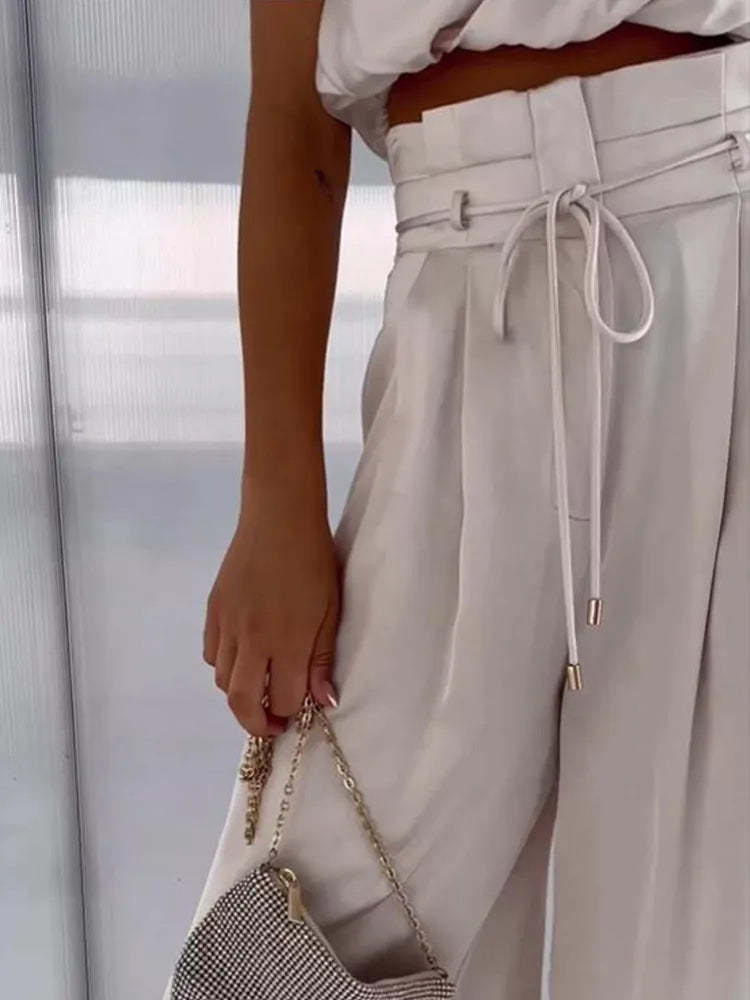 Close-up of cream draped pants showing high waist, pleated detail, and drawstring tie