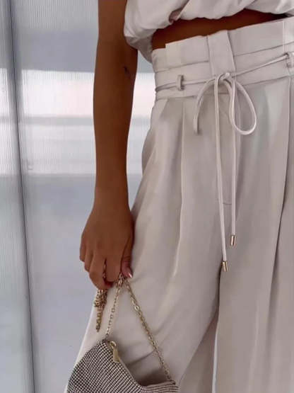 Close-up of cream draped pants showing high waist, pleated detail, and drawstring tie