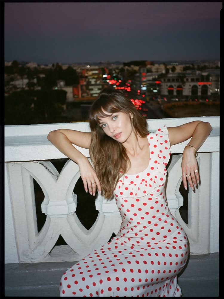 Red and white polka dot midi dress with ruffled off-shoulder design on model at dusk