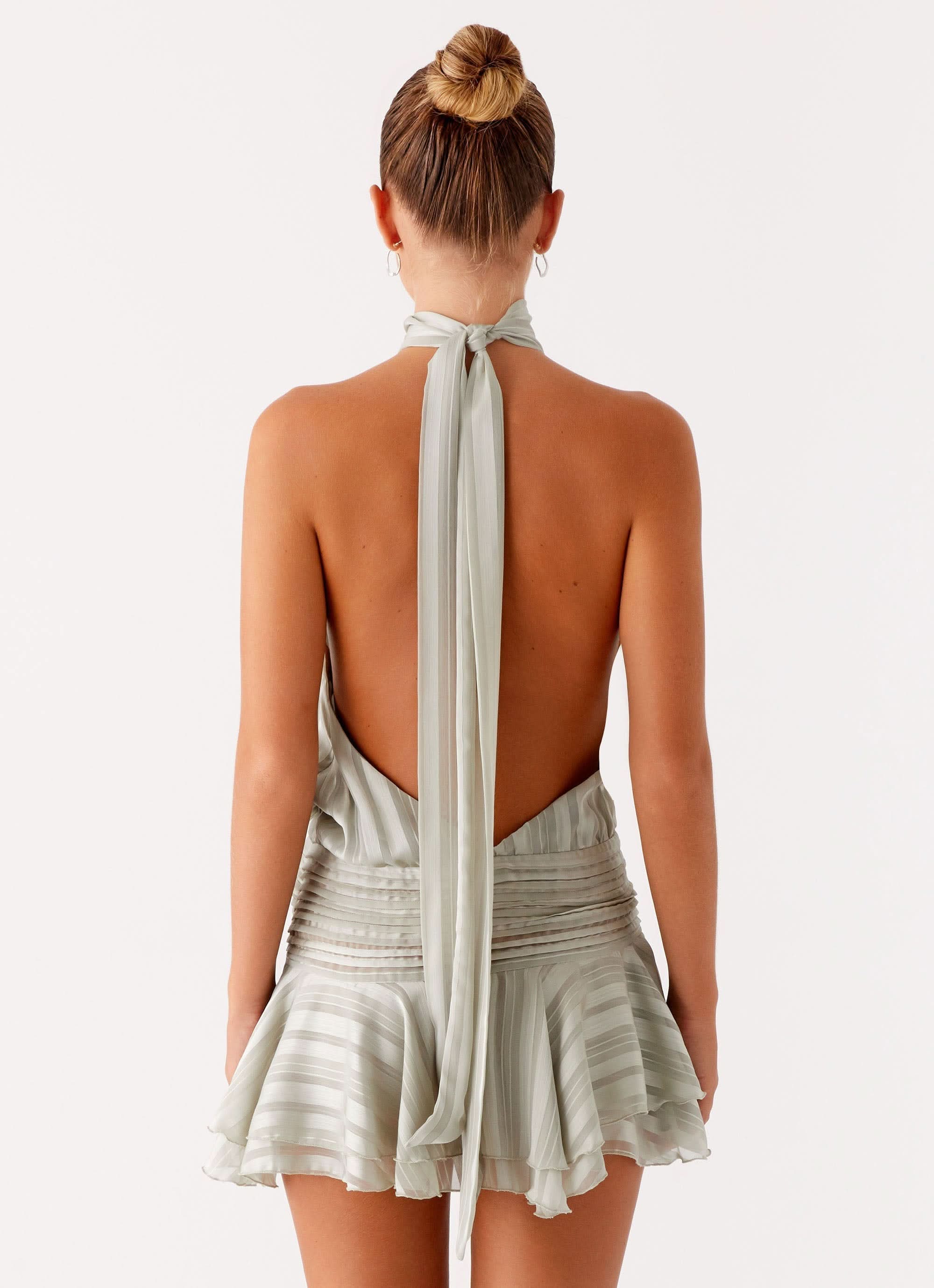 Rear view of sage ruffle mini dress showing open back with halter straps