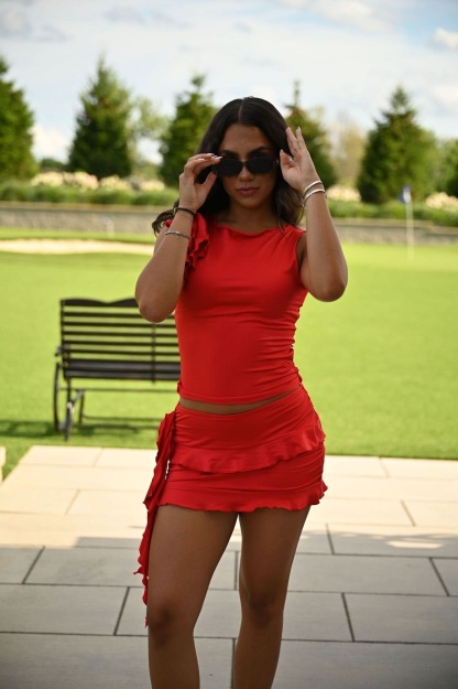 Close-up front view of red ruched tank with shoulder ruffle detail and matching mini skirt